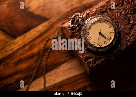 Auf dem Tisch steht eine alte Taschenuhr über einem alten Holzkoffer. Vintage Hintergrund aus einer Sammlung von Antiquitäten. Nahaufnahme und ausgewählter Fokus Stockfoto