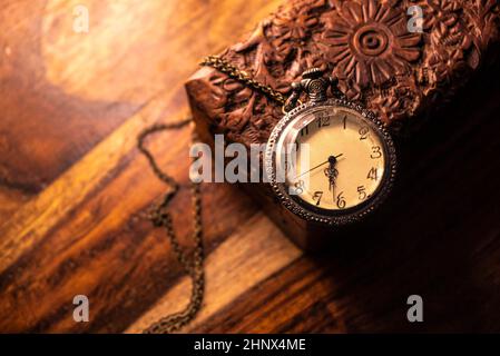 Auf dem Tisch steht eine alte Taschenuhr über einem alten Holzkoffer. Vintage Hintergrund aus einer Sammlung von Antiquitäten. Nahaufnahme und ausgewählter Fokus Stockfoto