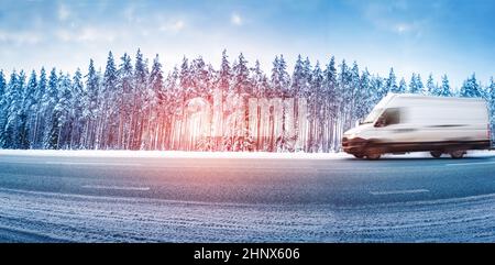 Weißer Van, der bei Schneefall auf einer rutschigen Asphaltstraße fährt. Fahrzeug fahren im Winter in weihnachten an schönen Morgen im Wald Stockfoto