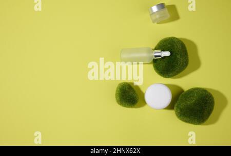 Weiße Glasflaschen mit einer Pipette auf grün-gelbem Hintergrund und Moosstücken. Kosmetik SPA Branding Mockup, Draufsicht Stockfoto