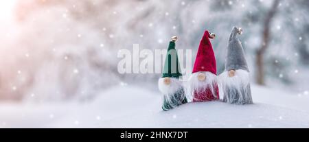 Drei niedliche Gnome in der Schneeverwehung im Winterwald bei Schneefall. Schöne Aussicht auf den verschneiten Hintergrund im Naturpark. Stockfoto