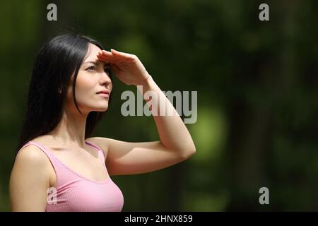 Konzentrierte asiatische Frau, die vor der Sonne schützt, mit der Hand, die in einem Park sucht Stockfoto