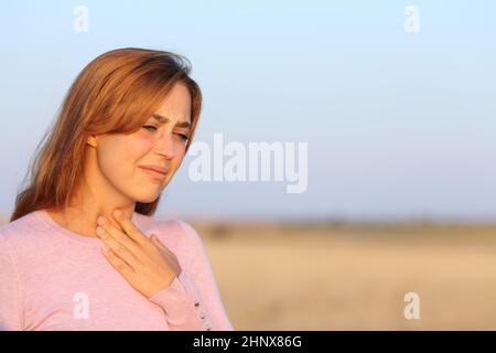 Gestresste Frau mit Halsschmerzen auf einem Feld Stockfoto