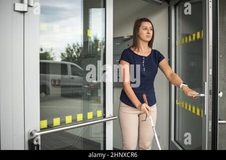 Junge Frau mit Sehbehinderung geht auf den Straßen der Stadt und nutzt ihren weißen Stock, um besser durch den städtischen Raum zu navigieren und sicher an ihr Ziel zu gelangen Stockfoto