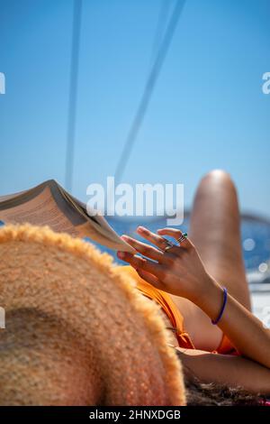 Reisenden Mädchen mit Vergnügen Lesen Buch und Sonnenbräune auf dem Segelboot. Aktive Sommerferien Genießen. Reisen nach Griechenland. Stockfoto