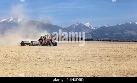 Tractor Pulling Metallwalzen über trockenes Gebiet mit Bergen im Hintergrund. Frühjahr Bodenvorbereitung. Stockfoto