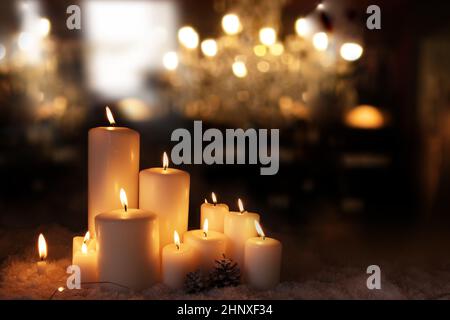 Brennende Kerzen im Schnee festlich dekoriert. Weihnachts- und Adventshintergrund mit goldenen Bokeh-Lichtern und kurzer Schärfentiefe. Platz für Text. Stockfoto