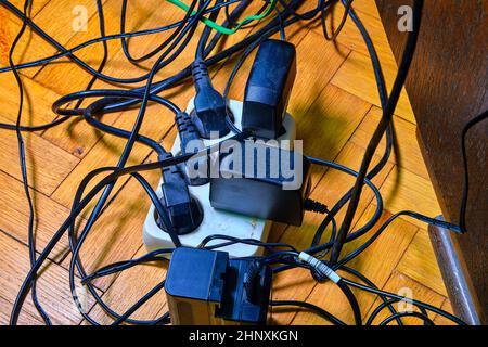 Kabelsalat und Batterie lädt auf parquete Stock. Haushaltsgeräte. Kabel Unordnung im heimischen Raum. Stockfoto