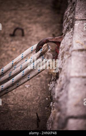 Alter rostiger Metallfestungsring an der Festungswand mit daran gebundenen Seilen. Stockfoto