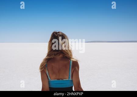 Rückansicht der blonden schönen kaukasischen jungen Frau in blau gekleidet Blick auf weißen Salzsee erstreckt sich bis zum Horizont mit klarem Himmel über Stockfoto