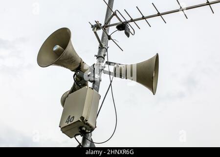 Public Address System Lautsprecher an einer Stange, die Antenne und die Box mit Nummer 46 teilweise abgeblättert, bewölkten Himmel im Hintergrund. Stockfoto