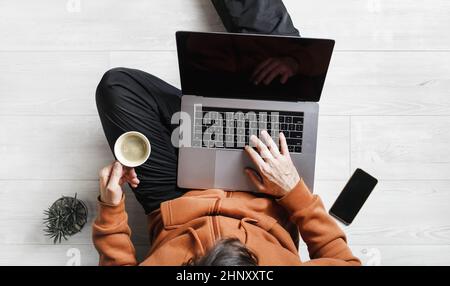 Während der Coronavirus-Pandemie arbeitet ein Geschäftsmann zu Hause. Freiberuflicher Mitarbeiter mit Laptop arbeitet, während er auf dem Boden sitzt. Online-Schulungen. Stockfoto