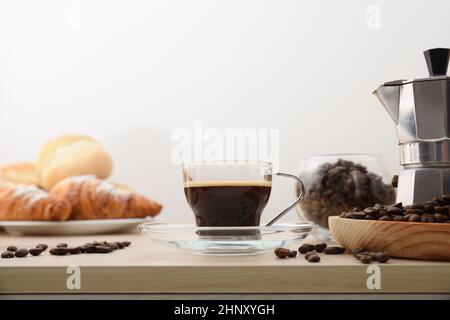 Italienischer Kaffee zum Frühstück auf Küchenbank mit Kaffeemaschine und Korb mit Gebäck Licht isoliert Hintergrund. Vorderansicht. Horizontale Zusammensetzung Stockfoto