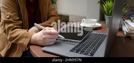 Nahaufnahme, freiberufliche Mitarbeiterin, die in einem Café arbeitet, die Details auf dem Laptop-Bildschirm sieht und ein tragbares Tablet verwendet. Stockfoto