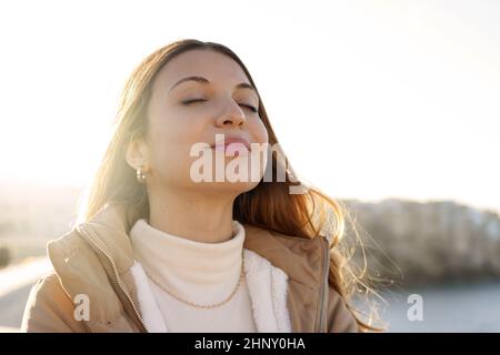 Junge charmante Frau atmet frische Luft und entspannt und lächelt bei Sonnenuntergang mit geschlossenen Augen Stockfoto