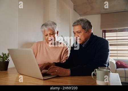 Ein älteres, multiethnisches Paar, das auf seinem Laptop nach Urlaubszielen sucht, während es zu Hause sitzt. Im Ruhestand und glücklich. Stockfoto