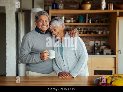Porträt eines lachenden älteren, pensionierten Birazialpaares, das sich umarmt, während es in der heimischen Küche steht. Stockfoto