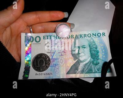 Schwedische Währung Hunderte von Banknoten und Münzen in der Hand. Dunkler Hintergrund. Stockfoto