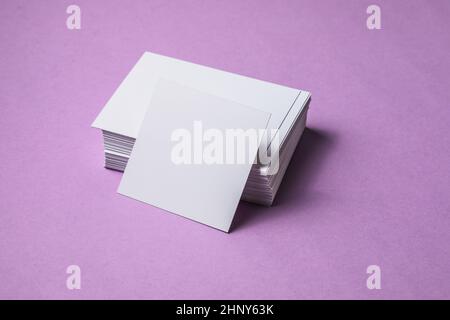 Weißes Laken-Modell. Stapel leerer Namenskarten. Leere weiße Visitenkarte auf violettem Papierhintergrund. Stockfoto