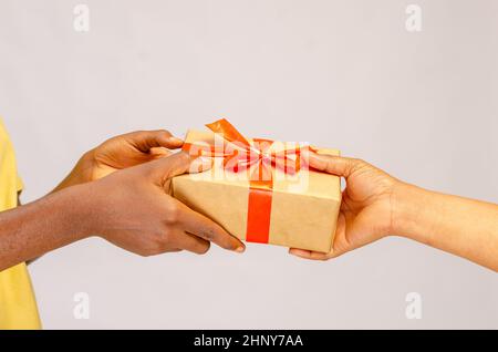 Konzept Der Feiertagsfeiertage. Nahaufnahme der weiblichen Hände, die ein Geschenk mit roter Schleife halten und der afroamerikanischen Frau eine Geschenkbox geben, Begrüßung mit Birthda Stockfoto