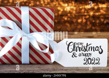 Ein Weihnachtsgeschenk mit Etikett mit englischer Kalligraphie Frohe Weihnachten und Ein glückliches 2022. Geschenkpapier mit Schleife und Licht im Hintergrund Stockfoto