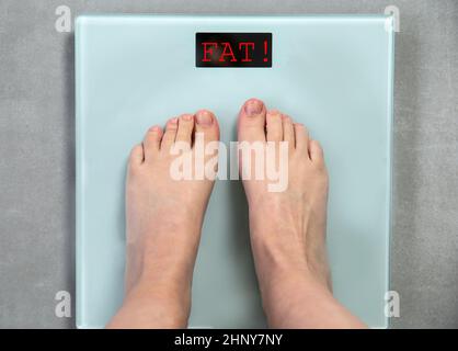 Füße auf digitaler Waage mit Wort FETT Draufsicht, Nachricht ungesunder Lebensstil, Gewicht zu verlieren Nachricht, Hilfe Konzept Nahaufnahme Stockfoto