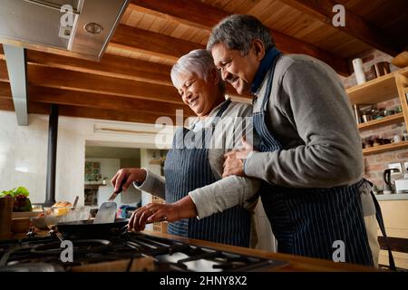 Ältere, multiethnische Paare lächeln, während sie in ihrer modernen Küche zusammen kochen. Glücklich und gesund im Ruhestand Stockfoto