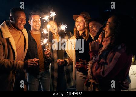 Eine vielfältige Gruppe multikultureller junger Erwachsener auf einer Party, bei der sie gemeinsam Wunderkerze erleuchten. Gute Zeiten, zusammen mit Freunden. Stockfoto