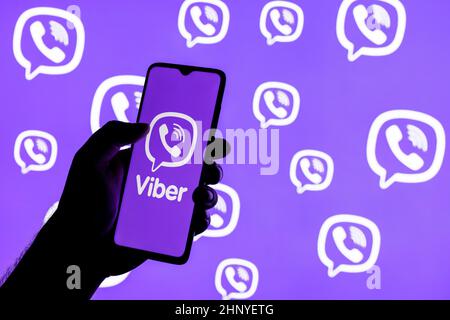 Smartphone mit Viber Instant Messaging Service-Logo auf dem Bildschirm in geballter Hand auf dem Hintergrund der Viber-Logos Stockfoto