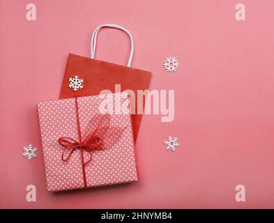 Nahaufnahme einer pinkgewickelten geschenkbox und einer roten Papiertüte auf dem Tisch, Tischansicht von oben, flach liegend Stockfoto