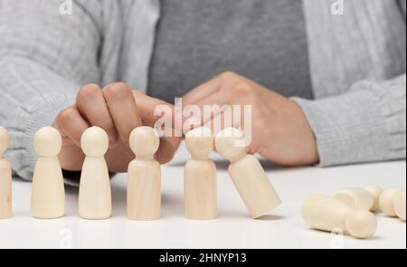 Hand stoppt den Fall von Holzfiguren von Männern auf weißem Hintergrund. Konzept einer starken und mutigen Persönlichkeit, die ungleich d aushalten kann Stockfoto