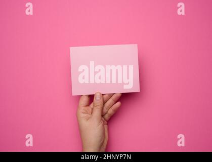 Weibliche Hand hält leeres rosa Papier auf einem rosa Hintergrund. Kopieren Bild oder Text einfügen, Nahaufnahme Stockfoto