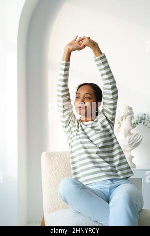 Junge afroamerikanische Frau, die sich während des Sitzens dehnt. Morgens schaute man sich das Fenster an Stockfoto