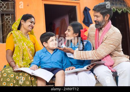 Traditionelle indische Eltern helfen ihren kleinen Kindern im Studium, Junge und Mädchen in der Schuluniform studieren zu Hause. Mutter trägt Sari und Vater in Stockfoto