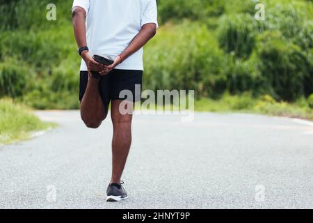 Nahaufnahme Asian junge Athlet Sport Läufer schwarz Mann tragen Uhr heben Füße Stretching Beine und Knie vor dem Laufen im Outdoor-Street Health Park, er Stockfoto