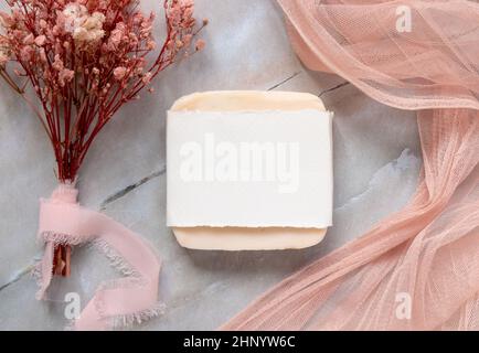 Handgemachte Seifenbar auf einem Marmortisch mit Papierverpackung, mit rosa Tüll Stoff und getrockneten Blumen um, Draufsicht. Seife mockup flach la Stockfoto