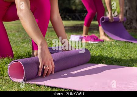 Zwei Frauen Rollen Pilates Matten in einem Park an einem sonnigen Tag im Sommer. Kaukasische Frauen in rosa Kleidung, die im Freien Sport treiben. Sport und gesundes Livestyl Stockfoto