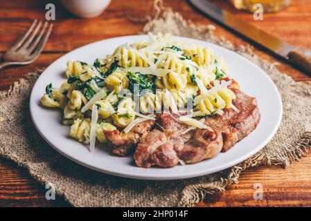 Schweinesteak und cremige Spinat-Pasta mit Parmesan-Käse garniert Auf weißem Teller Stockfoto