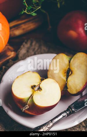 Zwei Hälften von rotem Apfel auf weißem Teller mit Vintage Messer in rustikaler Umgebung Stockfoto