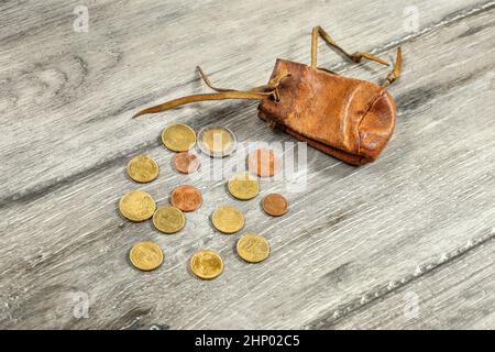 Alte abgenutzte Münze aus braunem Leder Tasche, mit Euro-münzen auf grau Holz Schreibtisch verschüttet. Stockfoto