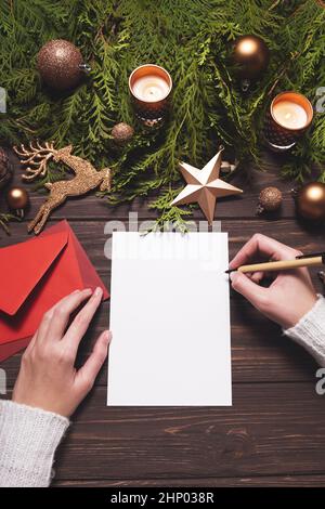 Frau, die einen Weihnachtsbrief mit Grußkarte oder Einladung auf Holzhintergrund schreibt. Modell, Draufsicht Stockfoto