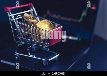 Seitenansicht Nahaufnahme Kryptowährung Konzept des Marktes Warenkorb voll von Bitcoin goldenen Krypto-Münzen stehen in der Nähe eines Notebook-Computer-Bildschirm mit tra Stockfoto
