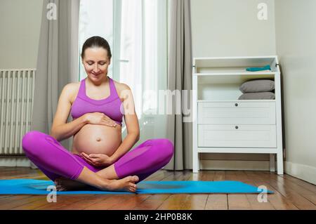 Schwanger in Sportkleidung halten Sie den Bauch auf der Yogamatte Stockfoto