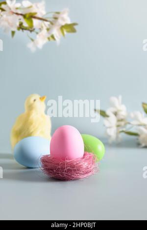 Osterfrühlingskomposition mit kleinem gelben Küken und bemalten Pastelleiern auf blauem Hintergrund. Frohe Ostern vertikale Grußkarte mit Kopierplatz. Stockfoto