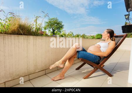 Die Schwangeren ruhen sich auf dem Balkon in einem Liegestuhl aus Stockfoto