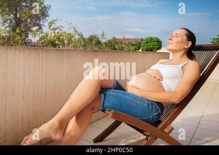 Die Schwangerin ruht sich auf dem Balkon im Liegestuhl aus Stockfoto