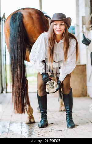 Vertikal lächelnd Pferdefrau Cowgirl, Bein. Sauber Schuh Hufpick, Reiten. Nahaufnahme Stockfoto