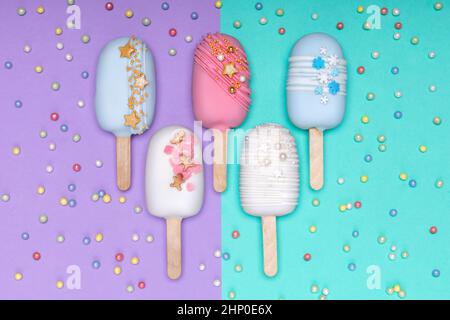 Auf violettem und türkisfarbenem Hintergrund werden Eiscreme mit dekorierten Kuchen serviert. Draufsicht. Stockfoto