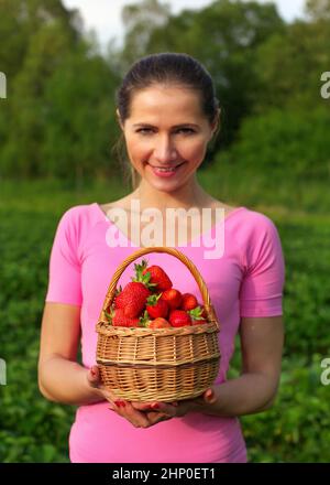 Junge Frau in Rosa holding Korb voller Erdbeeren nur aus dem Feld hinter ihr abgeholt. Flache Tiefenschärfe - Fokus auf Erdbeere nur Stockfoto