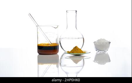 Eisenchlorid-Flüssigkeit mit Rührstab im Becher, kristallklare Flüssigkeit in Flachbodenflasche, organisches Curcuma-Pulver und weiße Flockenchemikalien. Schließenu Stockfoto